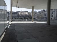 an empty concrete patio with white columns overlooking buildings and river in the middle of it