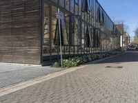 a narrow paved side walk near the entrance of a glass building with a parking meter in front of it