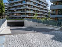 a brick road leads to a car tunnel that is part of a building complex with several balconies