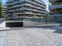 a brick road leads to a car tunnel that is part of a building complex with several balconies