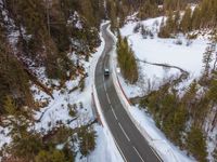 a truck driving along a narrow highway in the mountains with trees and snow on both sides