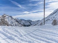 a snowy road with skis on it next to mountains under a blue sky with white clouds