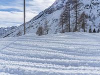a snowy road with skis on it next to mountains under a blue sky with white clouds