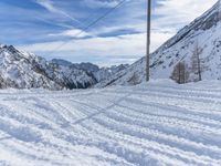 a snowy road with skis on it next to mountains under a blue sky with white clouds