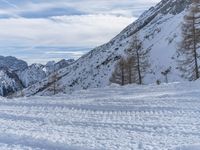 a snowy road with skis on it next to mountains under a blue sky with white clouds