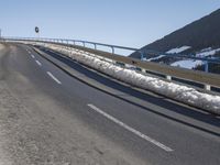 a motorcycle is driving down the snowy road next to snow covered hills on a sunny day