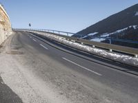 a motorcycle is driving down the snowy road next to snow covered hills on a sunny day