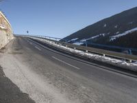 a motorcycle is driving down the snowy road next to snow covered hills on a sunny day