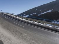 a motorcycle is driving down the snowy road next to snow covered hills on a sunny day