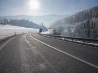 a road stretches across the snow covered landscape with mountain and forest in the background with sun shining