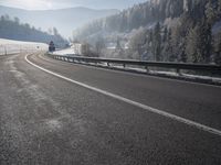 a road stretches across the snow covered landscape with mountain and forest in the background with sun shining