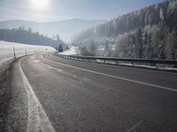 a road stretches across the snow covered landscape with mountain and forest in the background with sun shining