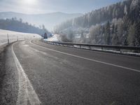a road stretches across the snow covered landscape with mountain and forest in the background with sun shining