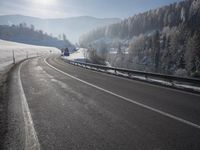 a road stretches across the snow covered landscape with mountain and forest in the background with sun shining