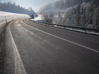 a road stretches across the snow covered landscape with mountain and forest in the background with sun shining