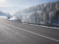 a road stretches across the snow covered landscape with mountain and forest in the background with sun shining