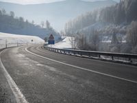 a road stretches across the snow covered landscape with mountain and forest in the background with sun shining