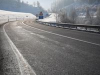a road stretches across the snow covered landscape with mountain and forest in the background with sun shining