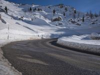 a snowy mountain side road with a steep hillside in the background and a blue sky