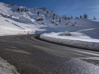 a snowy mountain side road with a steep hillside in the background and a blue sky