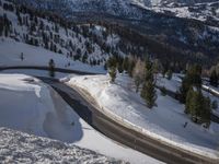 a winding road in the middle of a mountain covered in snow with trees and mountains