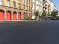 an empty street with buildings in the background and street lamps on each side, and red garage doors open