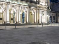 an empty square in front of a tall building at night near a bench at the curb