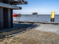 there is a small boat in the ocean near a dock with some buildings and yellow posts