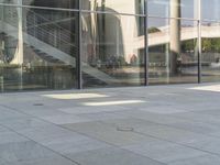 an open area of stone floor, with some large glass windows and people walking around it