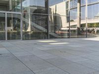 an open area of stone floor, with some large glass windows and people walking around it