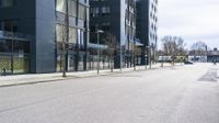 empty road with black buildings and buildings on side it and green bushes behind it with trees