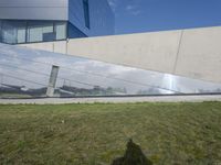 an empty green field in front of a big building with grass on both side and a glass paneled wall