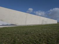an empty green field in front of a big building with grass on both side and a glass paneled wall