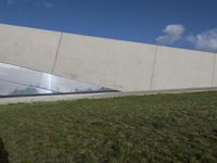 an empty green field in front of a big building with grass on both side and a glass paneled wall