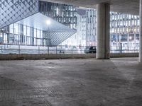 an empty parking garage at night with lots of windows and cement floors and some building behind it