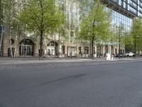 a paved city street with a building and trees in the background and cars parked on the side of it