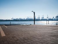 an empty public space in front of water and shipping dock with ships in the distance