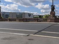 a person riding their bike across a bridge in front of buildings and blue sky with clouds