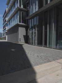 a sidewalk next to a building with glass doors and windows on the outside of it