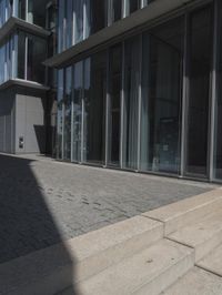 a sidewalk next to a building with glass doors and windows on the outside of it