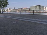 a bench with a bag on it near the water and city buildings in the background