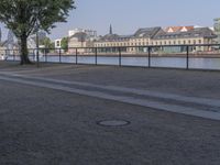 a bench with a bag on it near the water and city buildings in the background