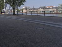 a bench with a bag on it near the water and city buildings in the background