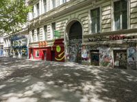 a restaurant in the middle of a narrow city street with graffiti on the wall and the sidewalk outside the building