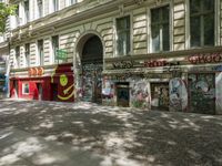 a restaurant in the middle of a narrow city street with graffiti on the wall and the sidewalk outside the building