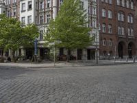 a city street is empty except for some people to use it - some buildings are next to a sidewalk with trees and bushes