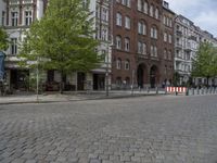 a city street is empty except for some people to use it - some buildings are next to a sidewalk with trees and bushes