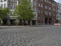 a city street is empty except for some people to use it - some buildings are next to a sidewalk with trees and bushes