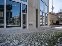 an empty street with a stone path near large building and a tv tower on the far side