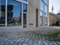 an empty street with a stone path near large building and a tv tower on the far side